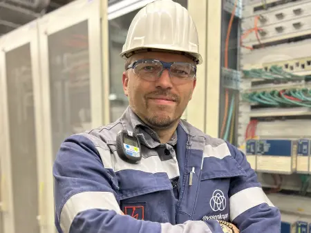 Jens Leurs wearing blue workwear with a helmet and thyssenkrupp logo in front of electrical equipment at thyssenkrupp Steel. Jens Leurs wearing blue workwear with a helmet and thyssenkrupp logo in front of electrical equipment at thyssenkrupp Steel.