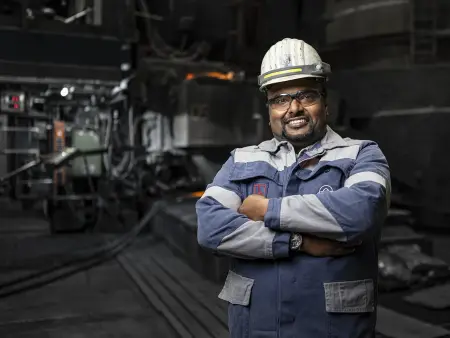 Nantheepan Kalanathan wearing blue workwear with reflective stripes and a helmet in an industrial setting at thyssenkrupp Steel. Nantheepan Kalanathan wearing blue workwear with reflective stripes and a helmet in an industrial setting at thyssenkrupp Steel.