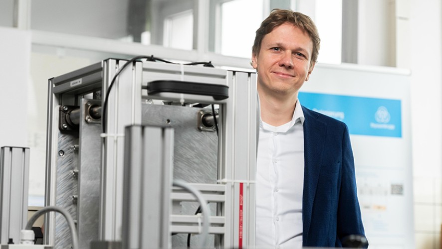 Ein Mitarbeiter von thyssenkrupp Steel steht hinter einer technischen Apparatur in einem Labor 