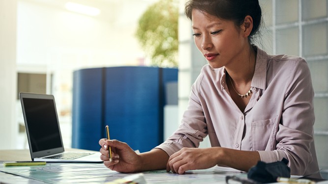 Eine Person sitzt in einem Büro an einem Schreibtisch mit Laptop und Unterlagen und arbeitet konzentriert.
