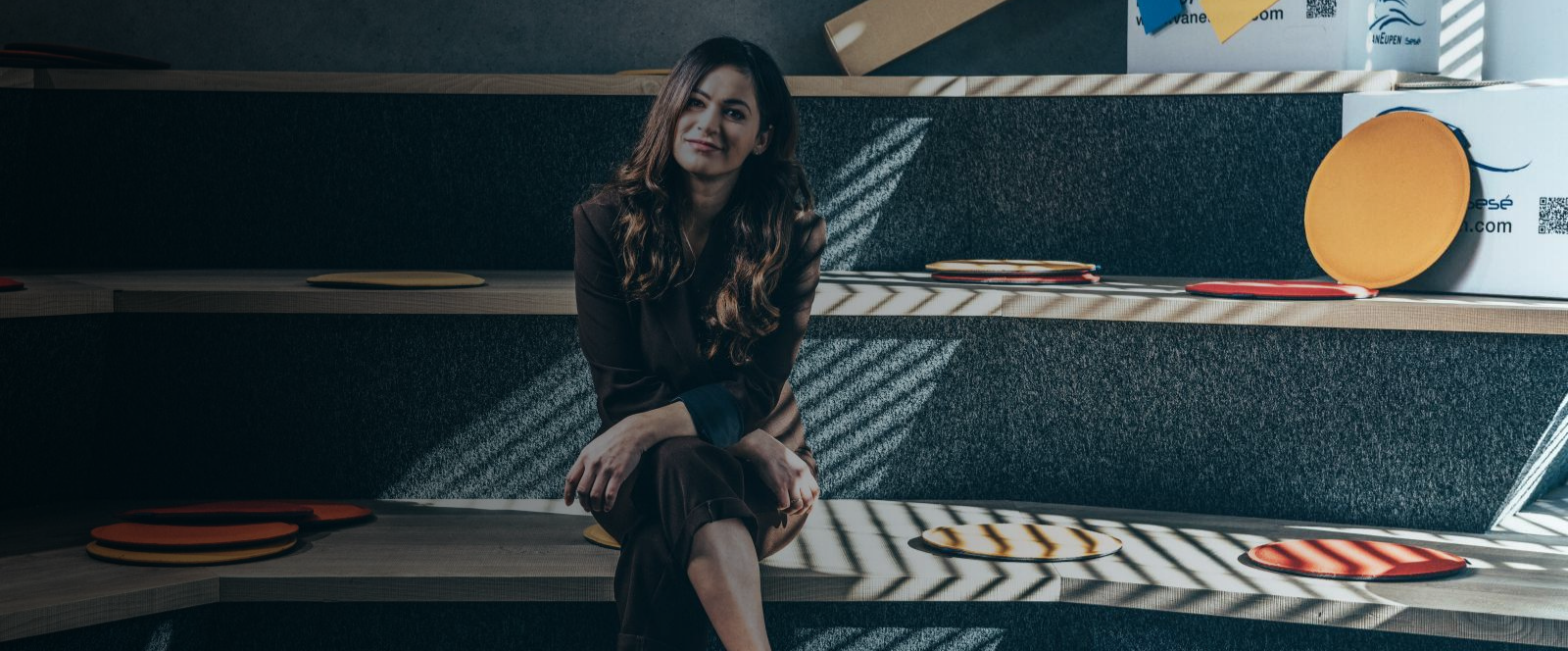 Eine Kollegin sitzt auf einer Treppe in einem modernen Büro, umgeben von runden Sitzkissen und Kartons.