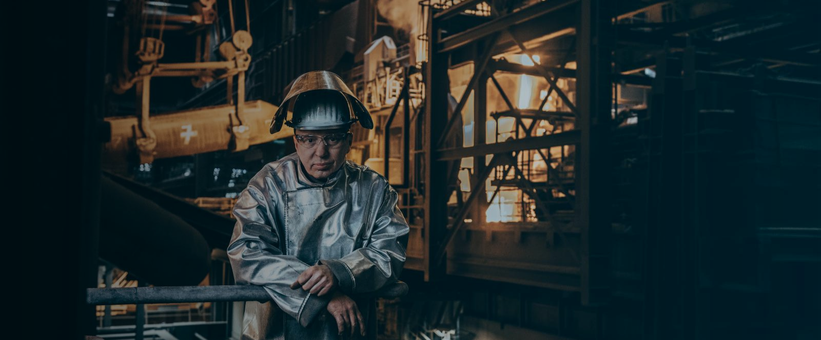 Ein Mitarbeiter von thyssenkrupp Steel in Schutzkleidung mit metallischem Anzug und Helm steht in einem industriellen Umfeld. Ein Mitarbeiter von thyssenkrupp Steel in Schutzkleidung mit metallischem Anzug und Helm steht in einem industriellen Umfeld.