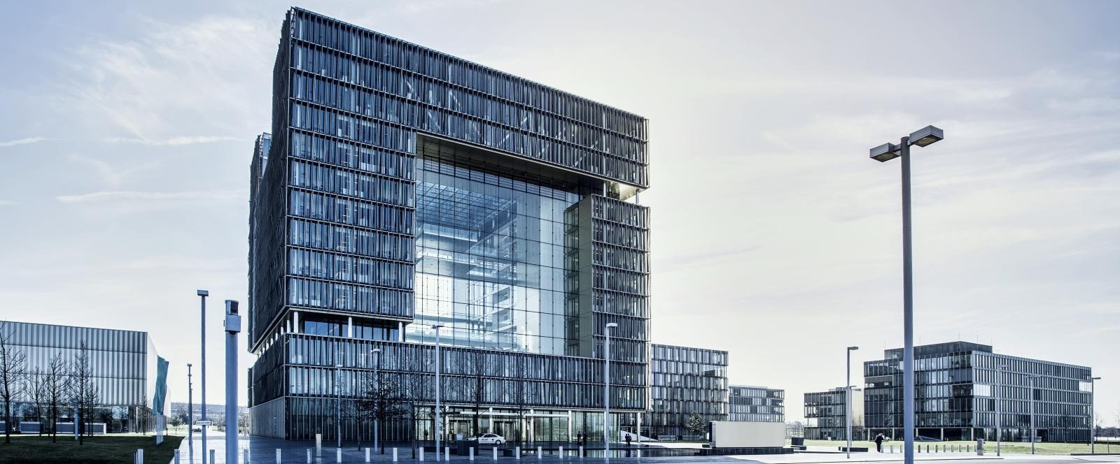 The thyssenkrupp Quartier of the AG in Essen with a central glass building, surrounding office buildings, and paved outdoor area under clear skies. The thyssenkrupp Quartier of the AG in Essen with a central glass building, surrounding office buildings, and paved outdoor area under clear skies.