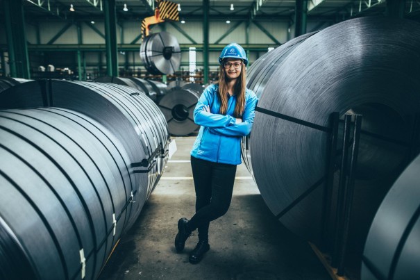 Mitarbeiterin bei thyssenkrupp in einem industriellen Umfeld mit Coils und Produktionsanlagen. Mitarbeiterin bei thyssenkrupp in einem industriellen Umfeld mit Coils und Produktionsanlagen.