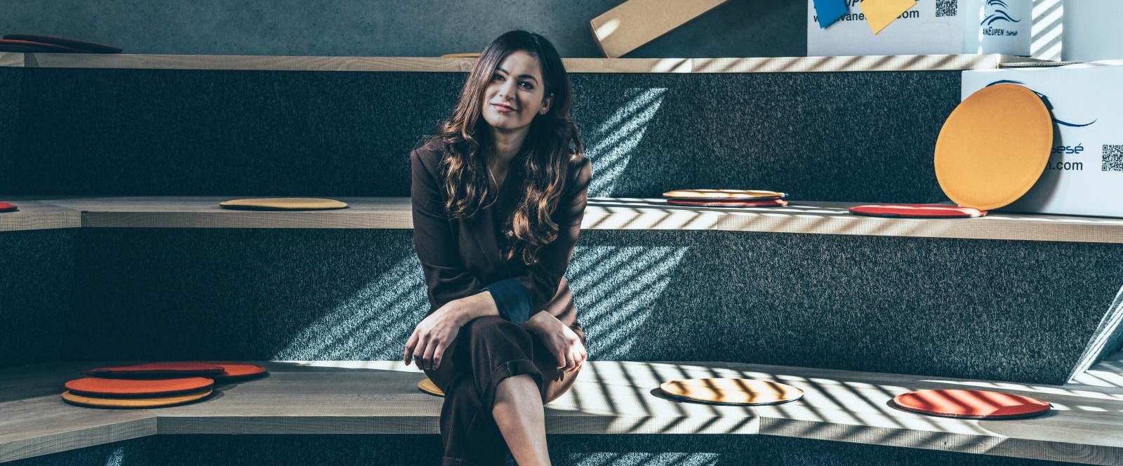 A colleague sits on a staircase in a modern office, surrounded by round seat cushions and cardboard boxes. A colleague sits on a staircase in a modern office, surrounded by round seat cushions and cardboard boxes.