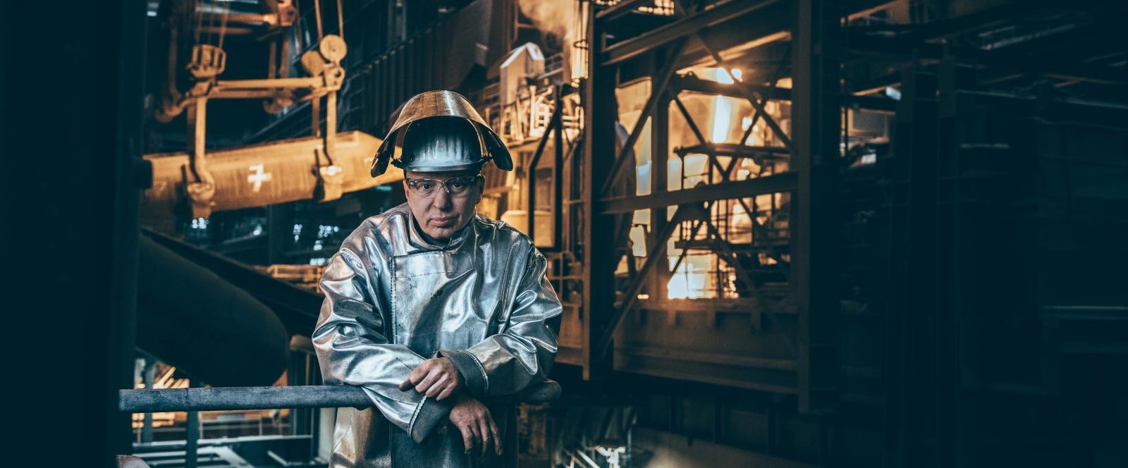 A thyssenkrupp Steel employee wearing protective clothing, including a metallic suit and helmet, stands in an industrial setting. A thyssenkrupp Steel employee wearing protective clothing, including a metallic suit and helmet, stands in an industrial setting.
