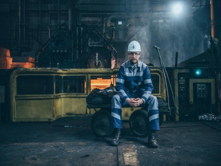 Mitarbeiter bei thyssenkrupp Steel in blau-weiß gestreifter Arbeitskleidung und weißem Helm in einem Werk mit Maschinen und Sicherheitsbarrieren. Mitarbeiter bei thyssenkrupp Steel in blau-weiß gestreifter Arbeitskleidung und weißem Helm in einem Werk mit Maschinen und Sicherheitsbarrieren.