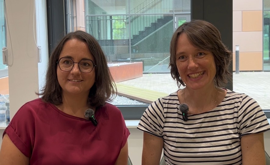 Anika Cornelius (links) und Sabine Hüwe (rechts) sitzen nebeneinander in einem Besprechungsraum. Im Hintergrund ist ein Fenster zu sehen. 