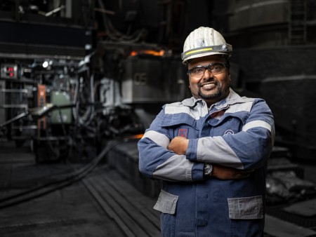 Nantheepan Kalanathan in blauer Arbeitskleidung mit reflektierenden Streifen und Helm in einem industriellen Umfeld bei thyssenkrupp Steel. 
