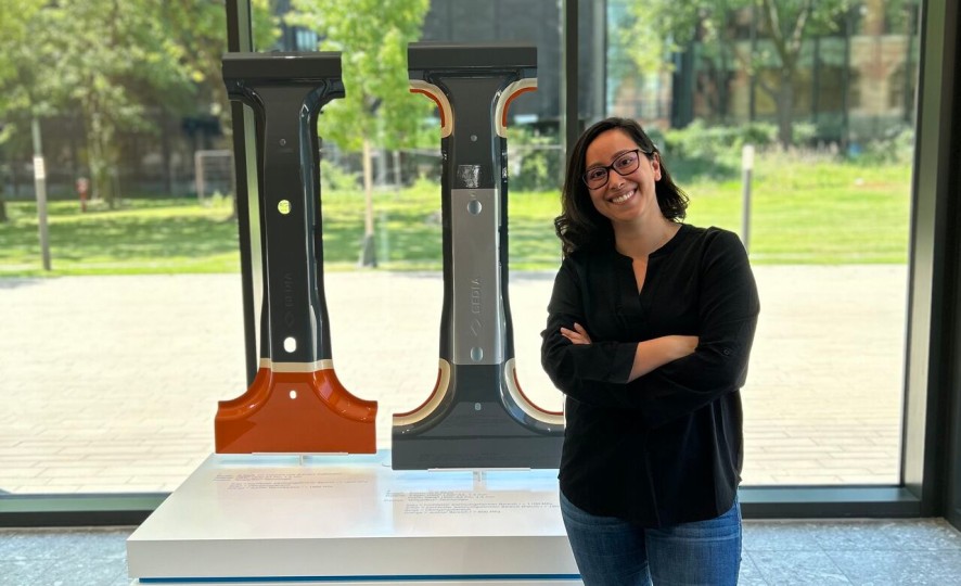 Cássia Castro Müller in front of a display with metal profiles and an information panel in the visitor area at thyssenkrupp Steel.