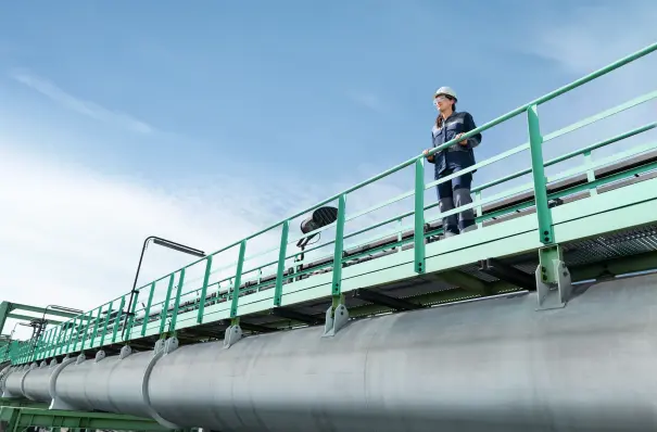 Employee at thyssenkrupp Steel on an elevated maintenance area above an industrial plant with piping. Employee at thyssenkrupp Steel on an elevated maintenance area above an industrial plant with piping.